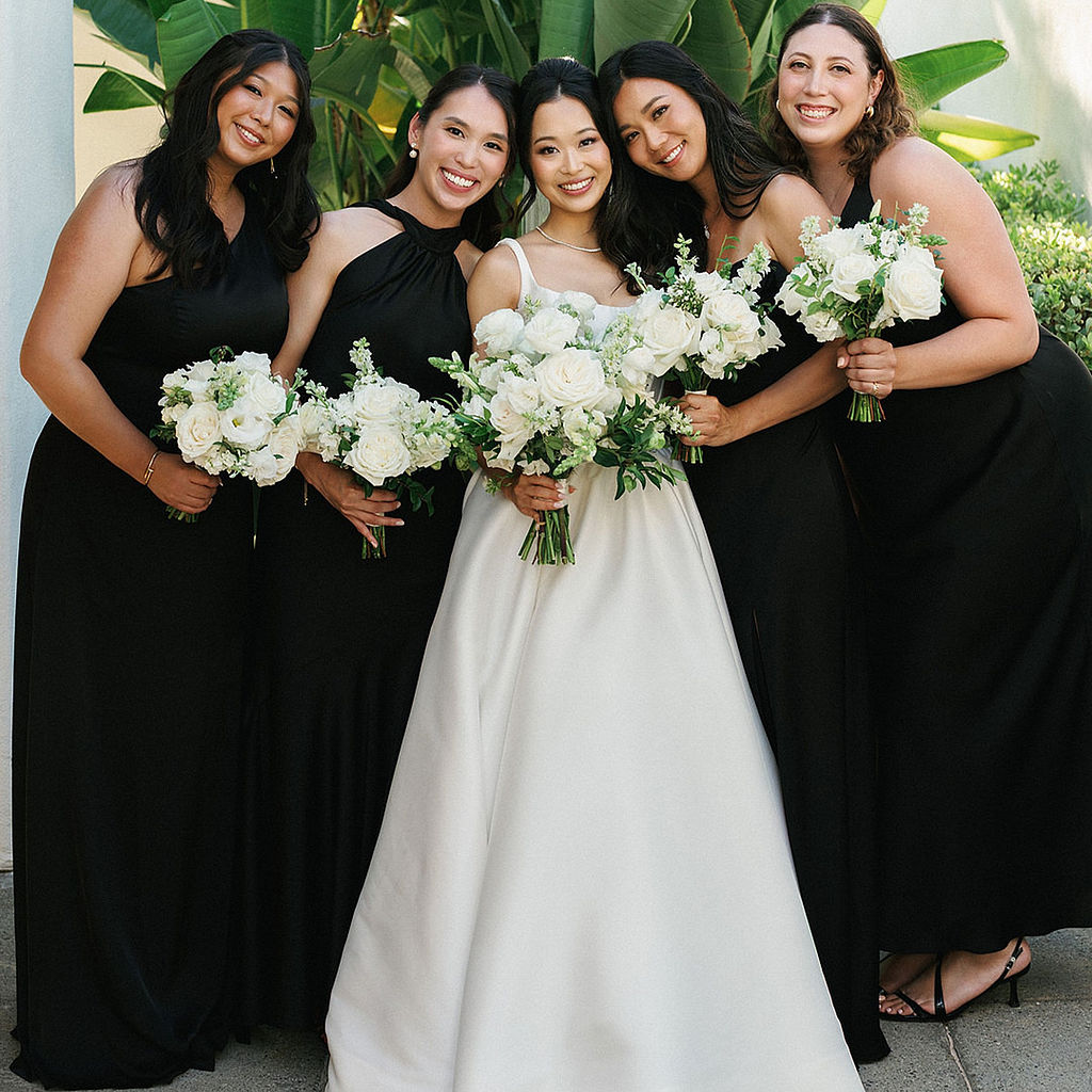 Bride with her four bridesmaids in floor-length black gowns, all holding white rose bouquets