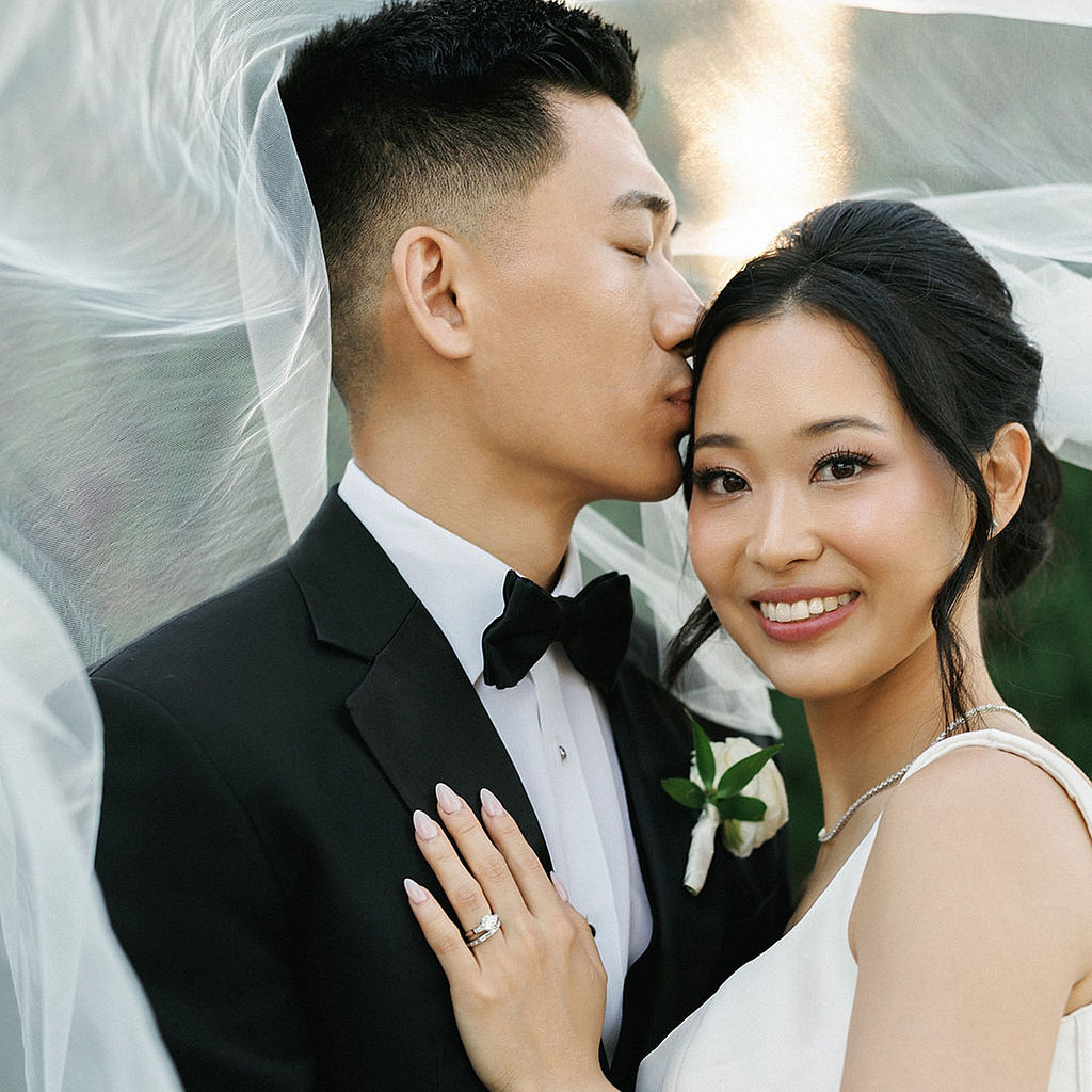 Bride and groom kissing on the fairway at golden hour, her lace-edged cathedral veil spread across the grass