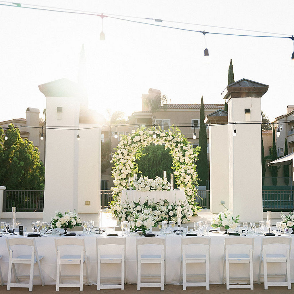 Terrace reception at Marbella Country Club with café lights, white folding chairs, and a sweetheart table under a white floral arch