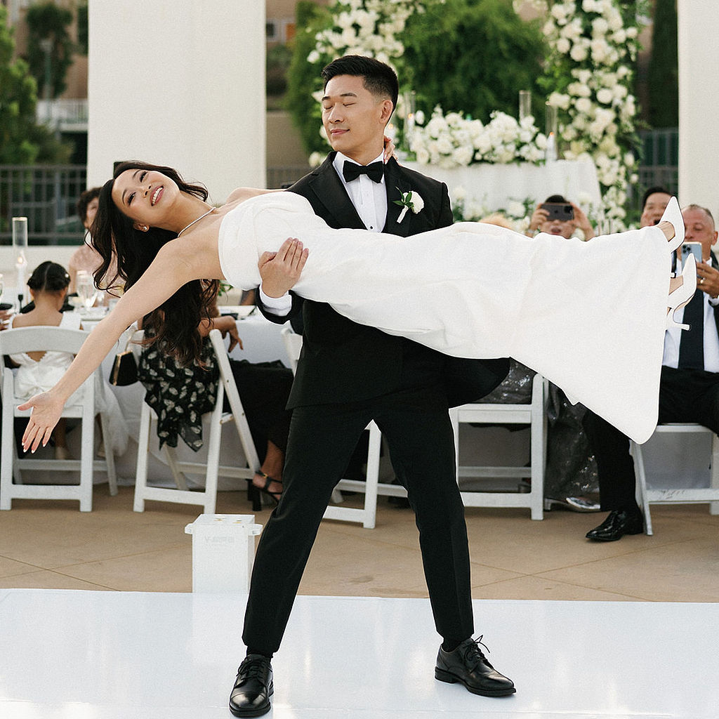 Groom lifting his bride horizontally during their first dance on a white dance floor