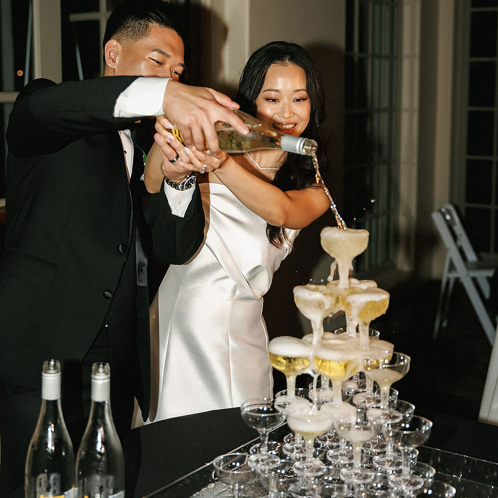 Bride and groom pouring champagne into a coupe tower together at Marbella Country Club